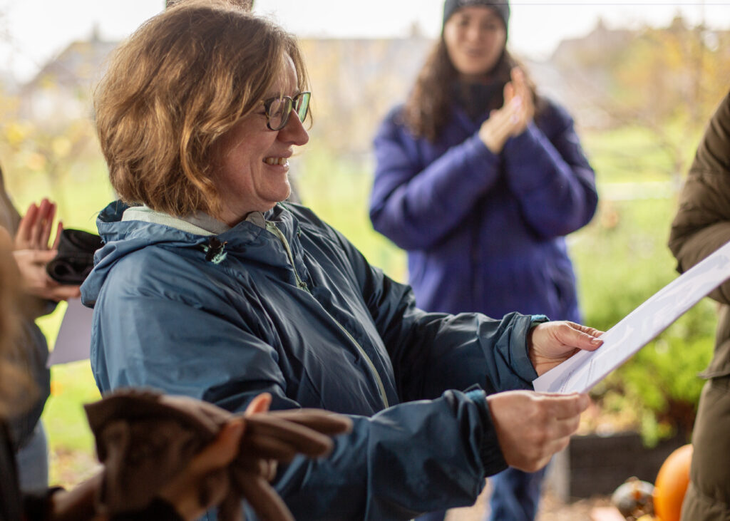 A woman smiling at a piece of paper she holds in her hands, people around her clapping their hands